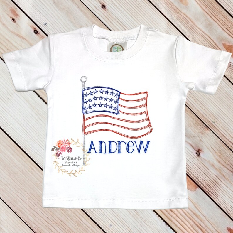 K&ouml;nnte beinhalten: Wei&szlig;es T-Shirt mit einer gestickten amerikanischen Flagge und dem Namen "Andrew" darunter.