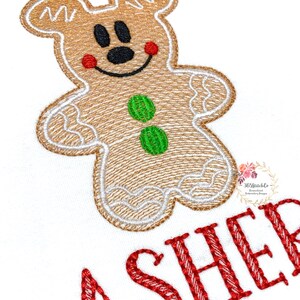 May include: Embroidered design of a gingerbread man with red cheeks, green buttons, and a smiling face. The text "ASHER" is embroidered in red below the gingerbread man.