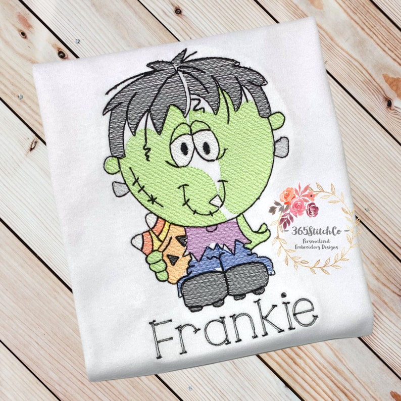 May include: A white t-shirt with an embroidered cartoon Frankenstein holding a candy corn. The text "Frankie" is embroidered below the image.