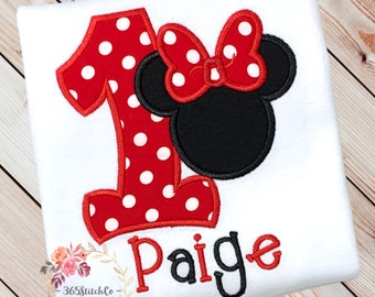 May include: Red and white polka dot number one with a black and red Minnie Mouse head and bow. The name Paige is embroidered below the number.