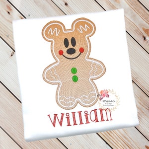 May include: A gingerbread man with Mickey Mouse ears, red cheeks, and green buttons. The gingerbread man is embroidered on a white shirt with the name "William" embroidered below.