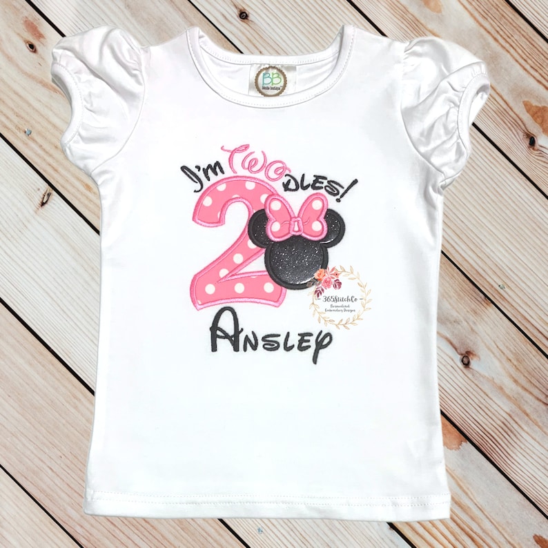 Puede incluir: Camiseta blanca de manga corta con el n&uacute;mero 2 de lunares rosas y blancos, una cabeza de Minnie Mouse negra y rosa y el texto "I'm Two-dles!" y "Ansley".