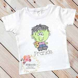 May include: White t-shirt with an embroidered cartoon Frankenstein holding a candy corn and the name Frankie.