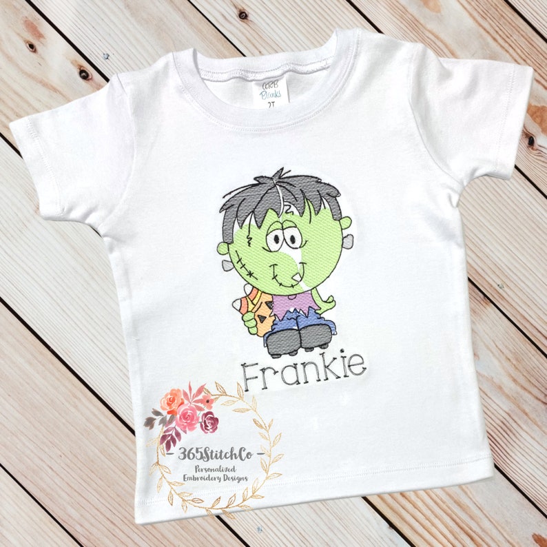 May include: White t-shirt with an embroidered cartoon Frankenstein holding a candy corn and the name Frankie.