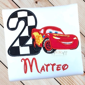 Pu&ograve; includere: T-shirt bianca con un'auto da corsa rossa e il numero 2 con un motivo a bandiera a scacchi. Il nome "Matteo" &egrave; scritto in rosso sotto la grafica. L'auto ha dettagli gialli e neri.