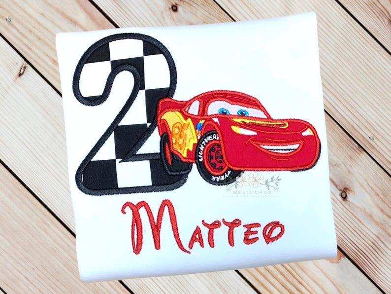 Pu&ograve; includere: T-shirt bianca con un'auto da corsa rossa e il numero 2 con un motivo a bandiera a scacchi. Il nome "Matteo" &egrave; scritto in rosso sotto la grafica. L'auto ha dettagli gialli e neri.