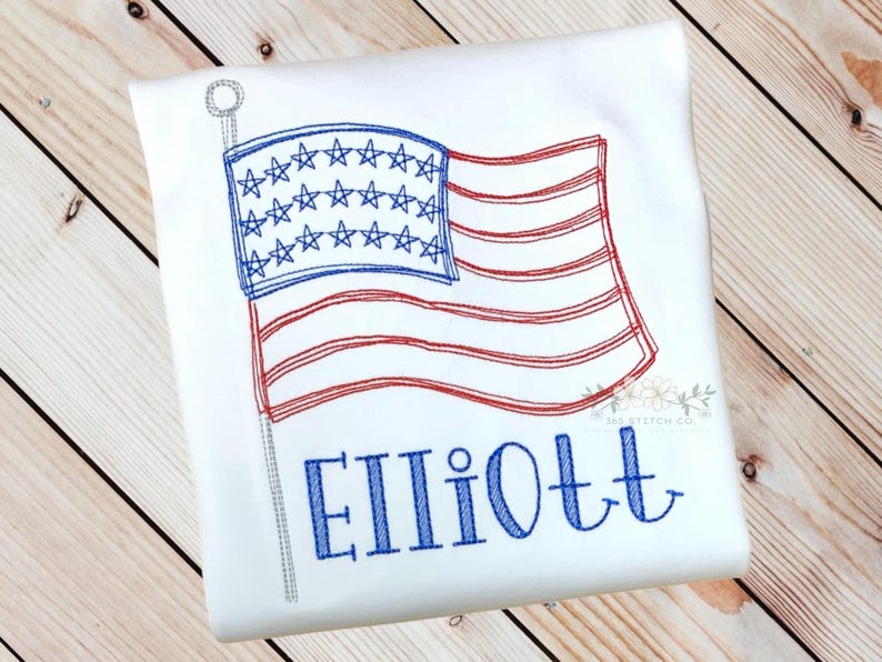 K&ouml;nnte beinhalten: Wei&szlig;es T-Shirt mit einer gestickten amerikanischen Flagge und dem Namen "Elliott" in blauer Farbe.