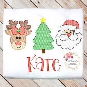 Puede incluir: Dise&ntilde;o bordado con un reno de nariz roja, un &aacute;rbol de Navidad verde y una cara de Pap&aacute; Noel blanca. El nombre "Kate" est&aacute; bordado en rojo debajo del dise&ntilde;o.