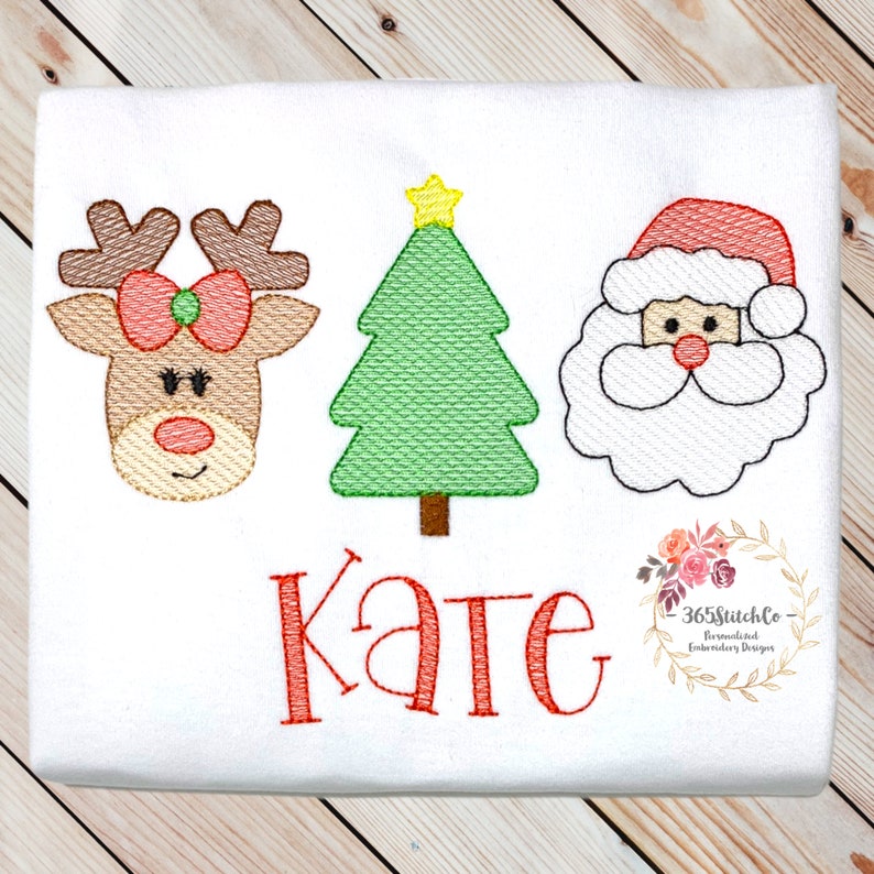 Puede incluir: Dise&ntilde;o bordado con un reno de nariz roja, un &aacute;rbol de Navidad verde y una cara de Pap&aacute; Noel blanca. El nombre "Kate" est&aacute; bordado en rojo debajo del dise&ntilde;o.