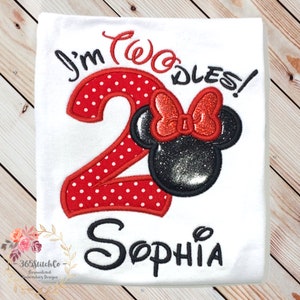 May include: A white t-shirt with red and black embroidery. The embroidery features a red number "2" with white polka dots, the words "I'm Two-dles!" and a black and red Minnie Mouse head. The name "Sophia" is embroidered in black below the number.