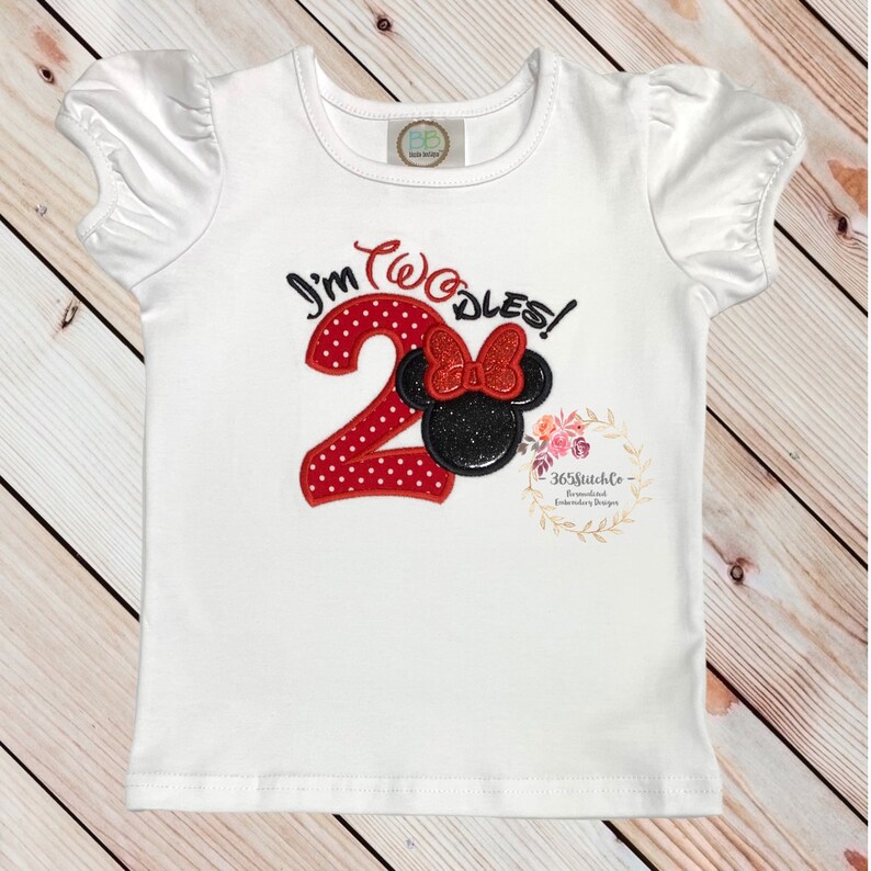 May include: White short-sleeved shirt with red and black embroidered design. The design features a red number "2" with white polka dots and a black Mickey Mouse head with a red bow. The text "I'm Two-dles!" is embroidered above the design.