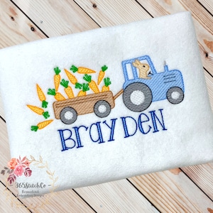 May include: Embroidered design of a blue tractor pulling a wagon full of carrots. A bunny is driving the tractor. The name "Brayden" is embroidered below the tractor.