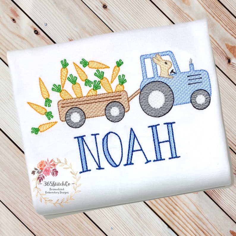 May include: A blue tractor with a brown wagon filled with orange carrots. A bunny is driving the tractor. The name NOAH is embroidered below the tractor.