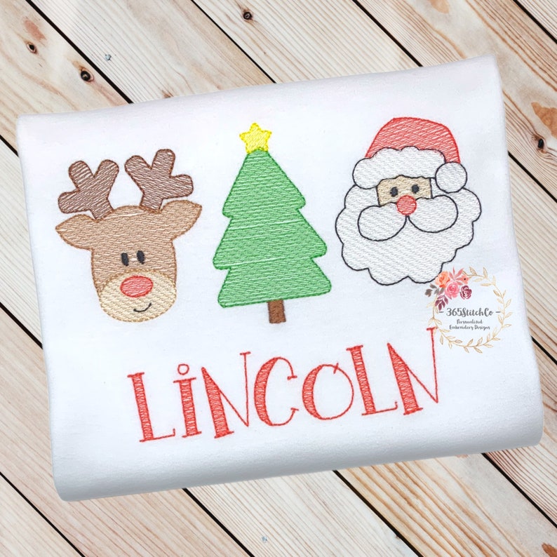 May include: Embroidered Christmas design featuring a reindeer, a Christmas tree, and Santa Claus. The design is in red, green, brown, and white. The name "LINCOLN" is embroidered below the design.