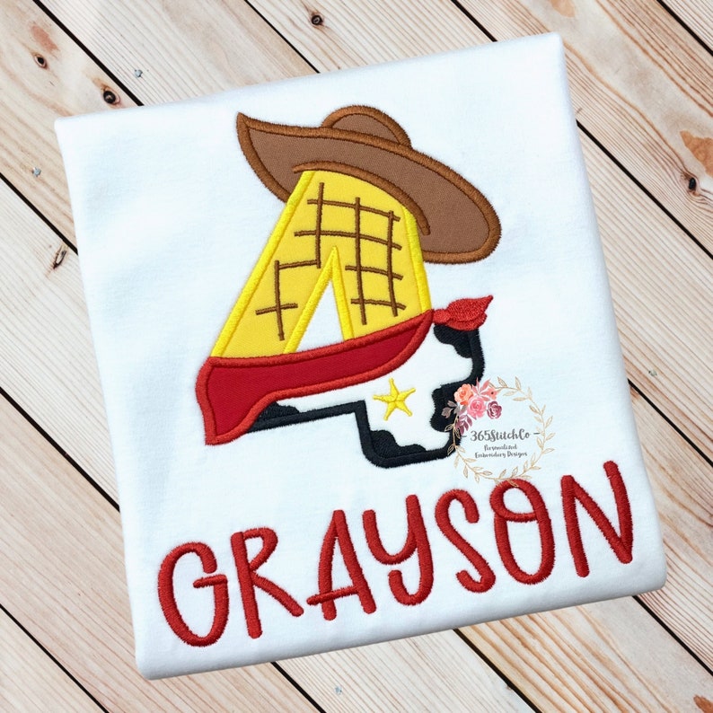 K&ouml;nnte beinhalten: Wei&szlig;es T-Shirt mit einer roten, gelben und braunen gestickten Nummer 4, einem Cowboyhut und einem Bandana. Der Name Grayson ist in Rot unter der Nummer gestickt.
