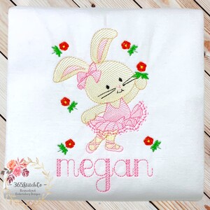 May include: Embroidered design of a ballerina bunny with a pink tutu and red flowers. The name "megan" is embroidered below the bunny.