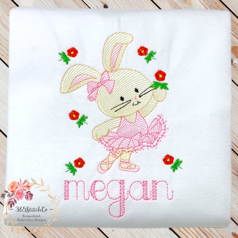 May include: Embroidered design of a ballerina bunny with a pink tutu and red flowers. The name "megan" is embroidered below the bunny.