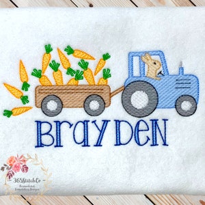 May include: A blue tractor with a bunny driver pulling a wagon full of orange carrots. The wagon has brown wheels and the tractor has gray wheels. The text "Brayden" is embroidered below the tractor.
