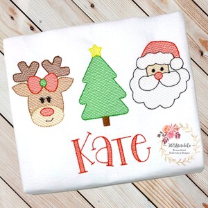 Puede incluir: Camiseta blanca bordada con tem&aacute;tica navide&ntilde;a con un reno rojo, un &aacute;rbol de Navidad verde y la cara de Pap&aacute; Noel. El nombre "Kate" est&aacute; bordado en rojo debajo de las im&aacute;genes.