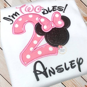 Puede incluir: N&uacute;mero dos de lunares rosa y blanco con una cabeza de Minnie Mouse negra y rosa y un lazo. El texto "I'm Twoodles!" est&aacute; por encima del n&uacute;mero y el nombre "Ansley" est&aacute; por debajo del n&uacute;mero.