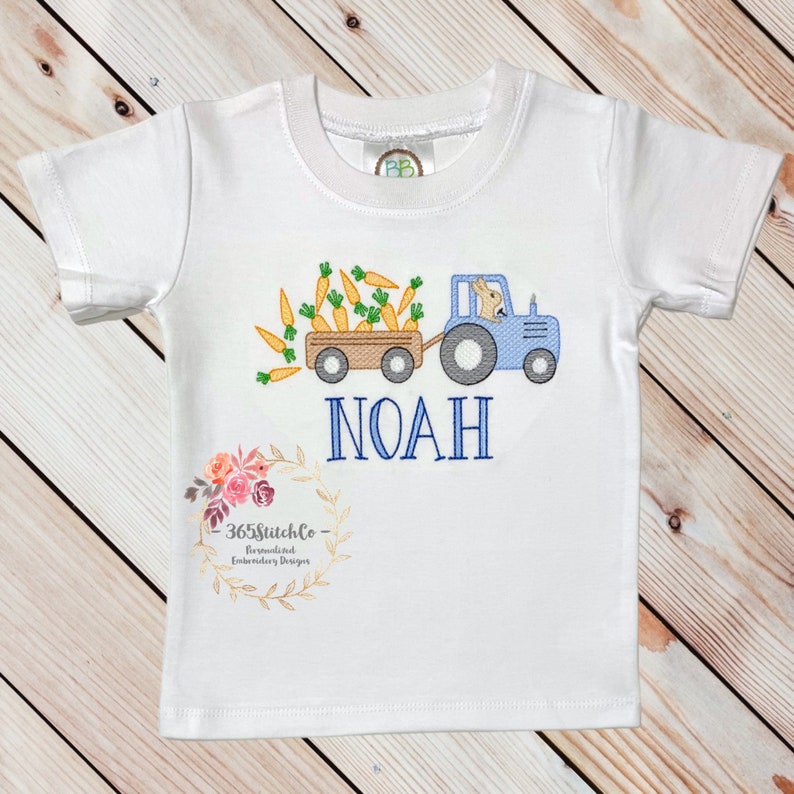 May include: White short-sleeved t-shirt with an embroidered design of a blue tractor pulling a wagon full of carrots. A bunny is driving the tractor. The name "NOAH" is embroidered below the tractor. The text "365stitchco - Personalized Embroidery Designs" is embroidered on the bottom of the shirt.