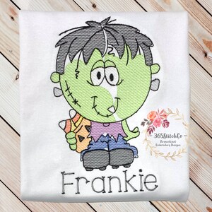 May include: Embroidered design of a green Frankenstein monster holding a candy corn. The monster has black hair, a purple shirt, blue jeans, and black shoes. The design includes the name "Frankie" in black lettering.