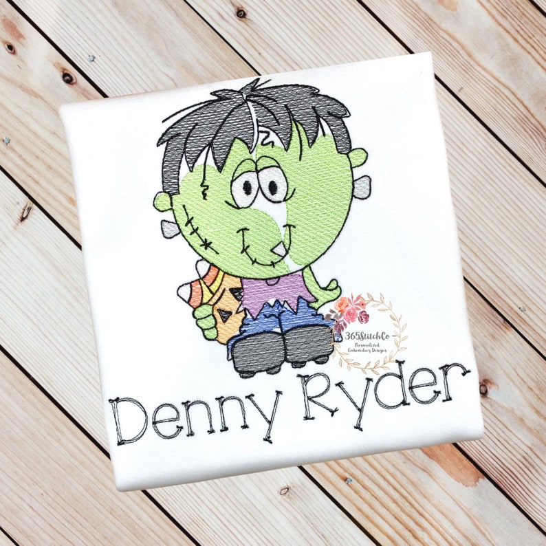 May include: A white t-shirt with an embroidered design of a green monster holding a candy corn. The text "Denny Ryder" is embroidered below the monster.