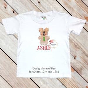May include: White t-shirt with an embroidered gingerbread man design and the name "ASHER" in red. The design is suitable for shirts sized 12M and 18M.