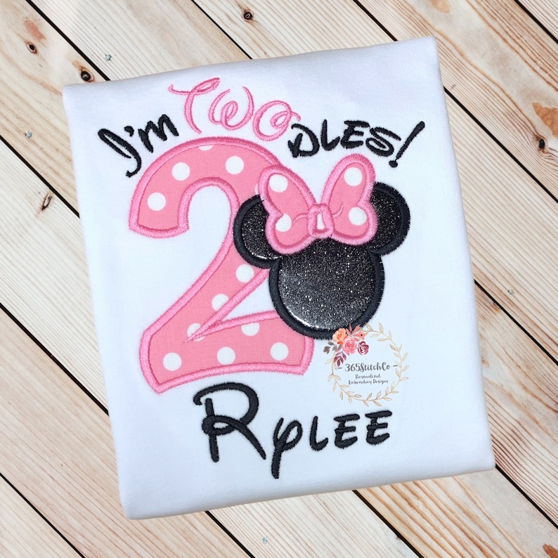 Puede incluir: N&uacute;mero dos rosa con lunares blancos y una cabeza de Minnie Mouse negra y blanca con un lazo rosa. El texto "I'm Two-dles!" est&aacute; por encima del n&uacute;mero y el nombre "Rylee" est&aacute; por debajo del n&uacute;mero.