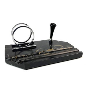 Könnte beinhalten: Ein schwarzer Schreibtisch-Organizer aus Marmor mit goldfarbener Maserung. Er verfügt über einen Stifthalter mit schwarzem Aufsatz, einen Briefhalter aus Chrom und eine rechteckige Basis mit Stufen. Ein stilvolles Büroaccessoire.
