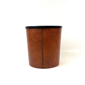 Può includere: Un cestino per la spazzatura in pelle marrone con un coperchio in plastica nera.