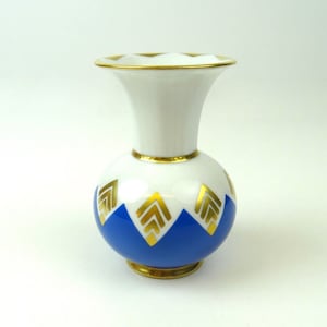 Könnte beinhalten: Eine kleine, weiße Porzellanvase mit einem blauen und goldenen geometrischen Muster. Die Vase hat einen runden Körper und eine ausgestellte Öffnung.