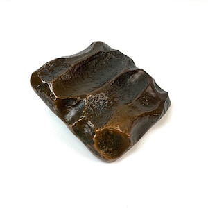 Peut inclure: Un plat carré en céramique de couleur brun foncé, texturé, avec trois lignes enfoncées. Le plat est fait pour ressembler à un rocher.