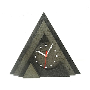 Puede incluir: Un reloj negro en forma de triángulo con una esfera blanca y agujas rojas. El reloj está hecho de metal y tiene una superficie texturizada.