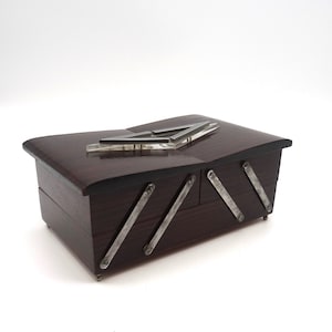 May include: A dark wood jewellery box with a silver metal design on the lid and silver metal accents on the sides.