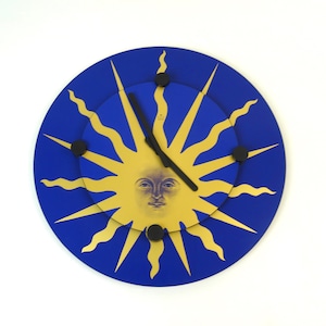 Könnte beinhalten: Eine blaue und goldene Uhr mit einem Sonnen-Gesichtsdesign. Die Uhr hat schwarze Zeiger und einen schwarzen Rand.