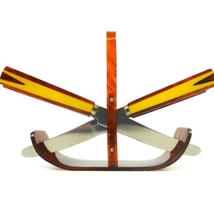 May include: A set of two vintage knives with yellow and brown Bakelite handles, displayed in a matching brown Bakelite stand.