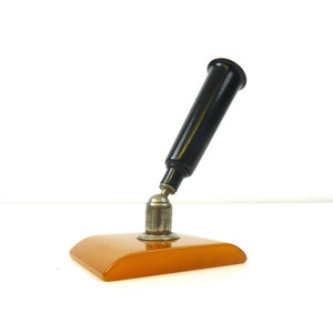 May include: A vintage orange and black desk pen holder. The pen holder has a black pen with a silver top and a round orange base.