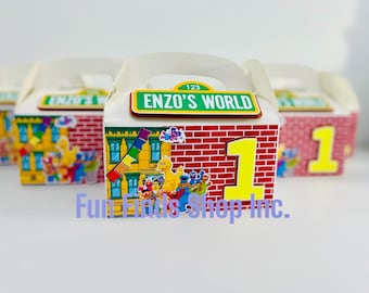 Puede incluir: Cajas de regalo de cartón blanco con asas que presentan un patrón de ladrillo rojo, un número uno grande de color amarillo y una señal de calle verde que dice 123 ENZO'S WORLD. Las cajas muestran gráficos coloridos de personajes de Sesame Street.