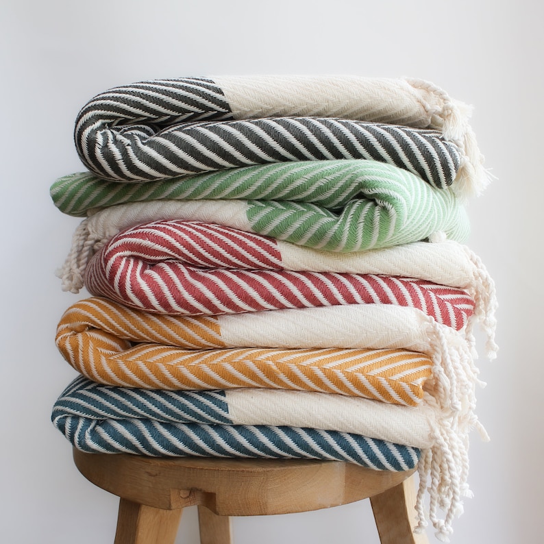 May include: A stack of five striped towels in various colors, including green, red, yellow, and blue, folded and arranged on a wooden stool.