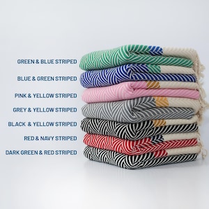 May include: A stack of eight striped Turkish towels in various color combinations, including green and blue, blue and green, pink and yellow, grey and yellow, black and yellow, red and navy, and dark green and red.