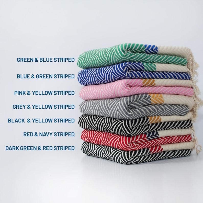 May include: A stack of eight striped Turkish towels in various color combinations, including green and blue, blue and green, pink and yellow, grey and yellow, black and yellow, red and navy, and dark green and red.