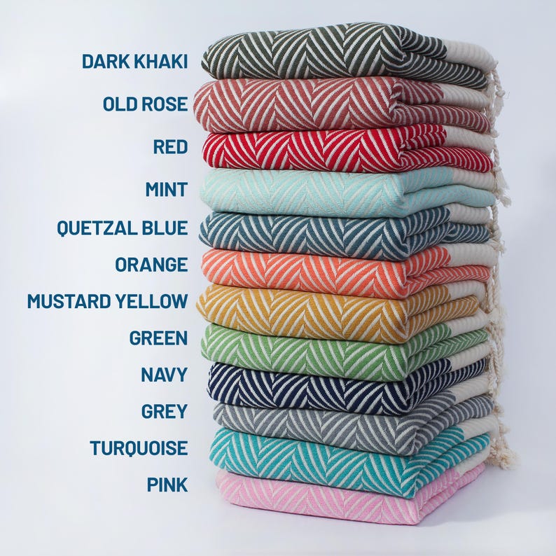 May include: A stack of 12 colorful Turkish towels with a chevron pattern. The towels are folded and stacked in order from dark khaki to pink. The colors are dark khaki, old rose, red, mint, quetzal blue, orange, mustard yellow, green, navy, grey, turquoise, and pink.