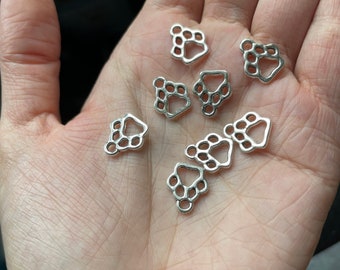 May include: A collection of silver-toned metal paw print charms. The charms are small and delicate, with a simple design.