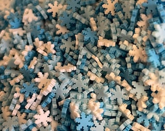 May include: A close-up image of a pile of blue and white snowflake sprinkles. The sprinkles are made of plastic and are perfect for decorating cakes, cupcakes, and other desserts.