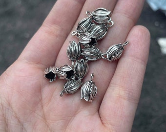 May include: A group of silver metal flower-shaped bead caps. The caps have a textured surface and a small loop at the top for attaching to jewelry.