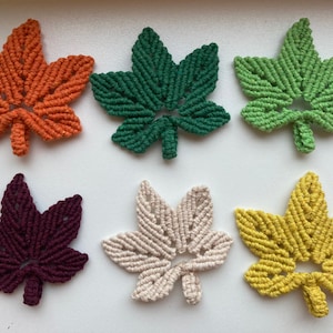 May include: Six handmade macrame leaf wall hangings in various colours, including orange, green, cream, and burgundy.