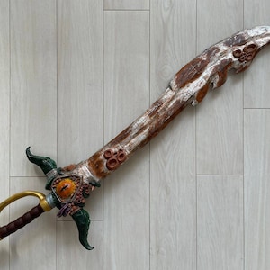 May include: A decorative sword with a wooden handle and a silver blade. The blade is decorated with a brown, orange, and green design. The sword has a gold handle and a brown leather grip.