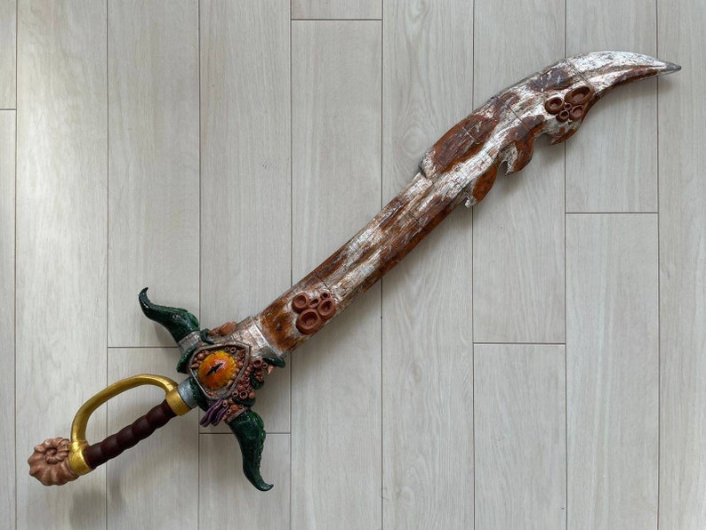 May include: A decorative sword with a wooden handle and a silver blade. The blade is decorated with a brown, orange, and green design. The sword has a gold handle and a brown leather grip.