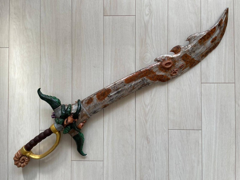 May include: A decorative sword with a rusty metal blade and a green and gold handle. The handle is decorated with a serpent-like design.